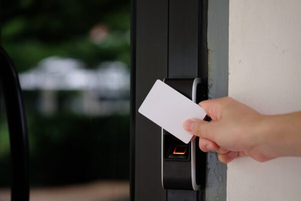 Person swiping white access card at electronic entry reader next to fingerprint scanner